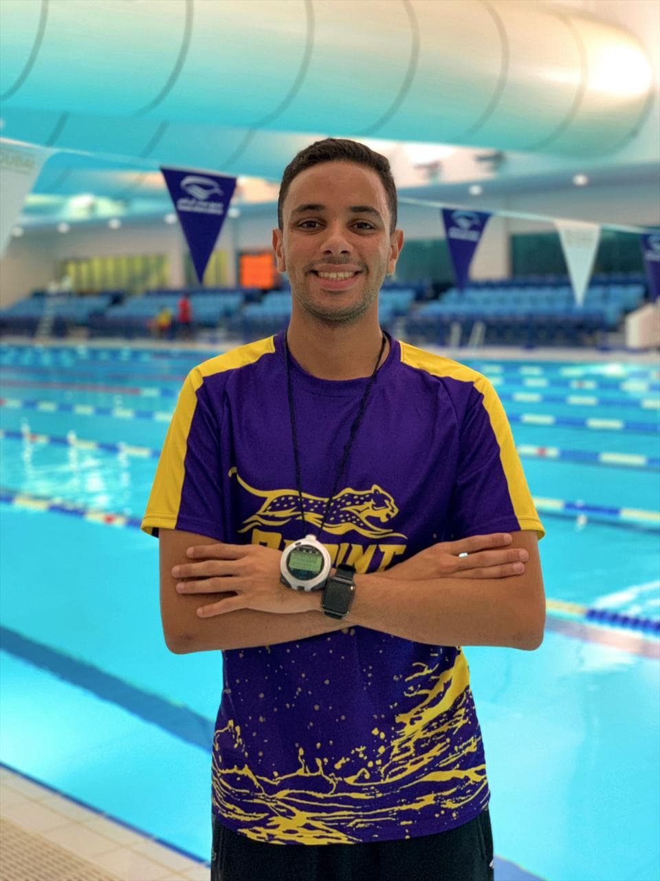 Coach Seif Aly standing poolside with a stopwatch around his neck
